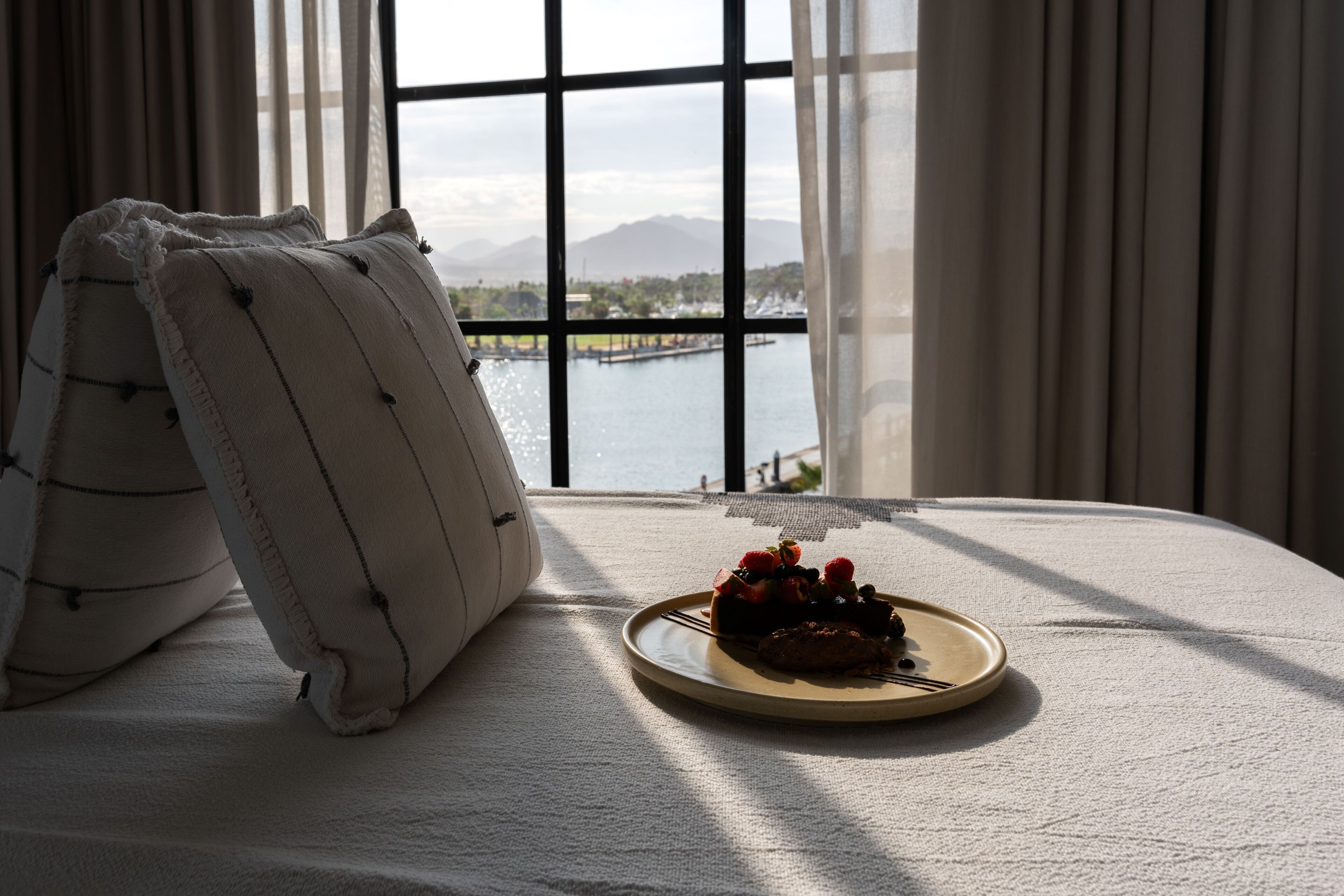 Una cama con vista a un lago y montañas a través de una ventana.