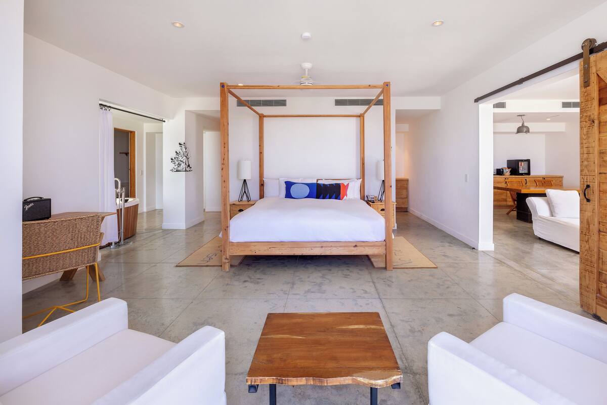 A spacious bedroom with a four-poster bed, a wooden coffee table, and white furniture.