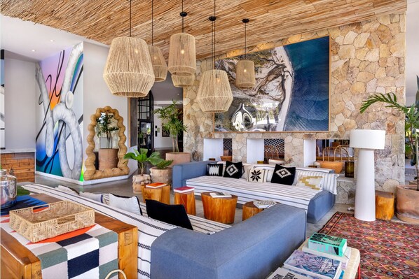 A modern lobby with a stone wall, woven light fixtures, a large abstract painting, and a seating area with patterned cushions. - Hotel El Ganzo - Adults Only (San José del Cabo)
