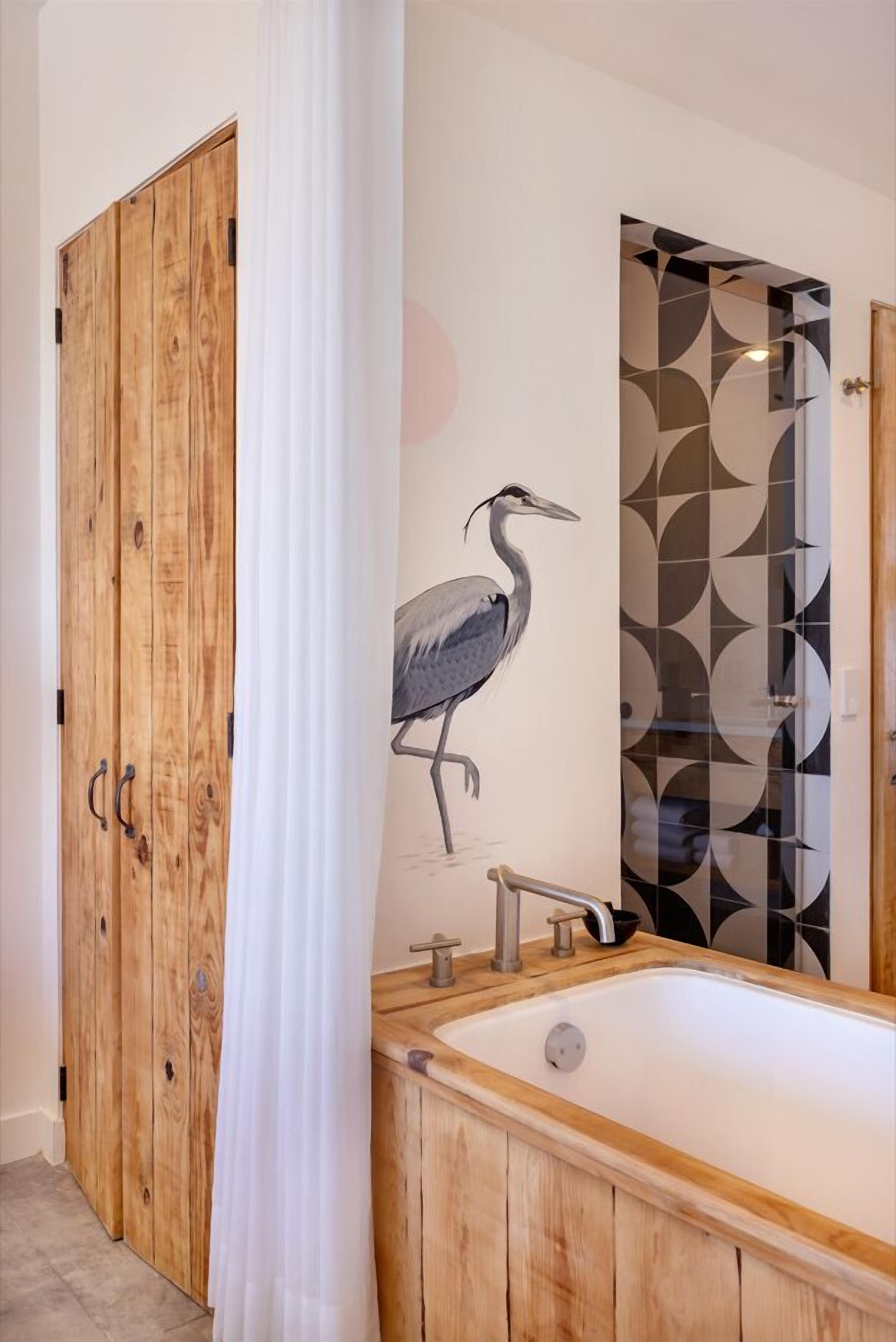 A bathroom with a wooden bathtub, a wooden wardrobe, and a wall with a geometric pattern and a bird mural.