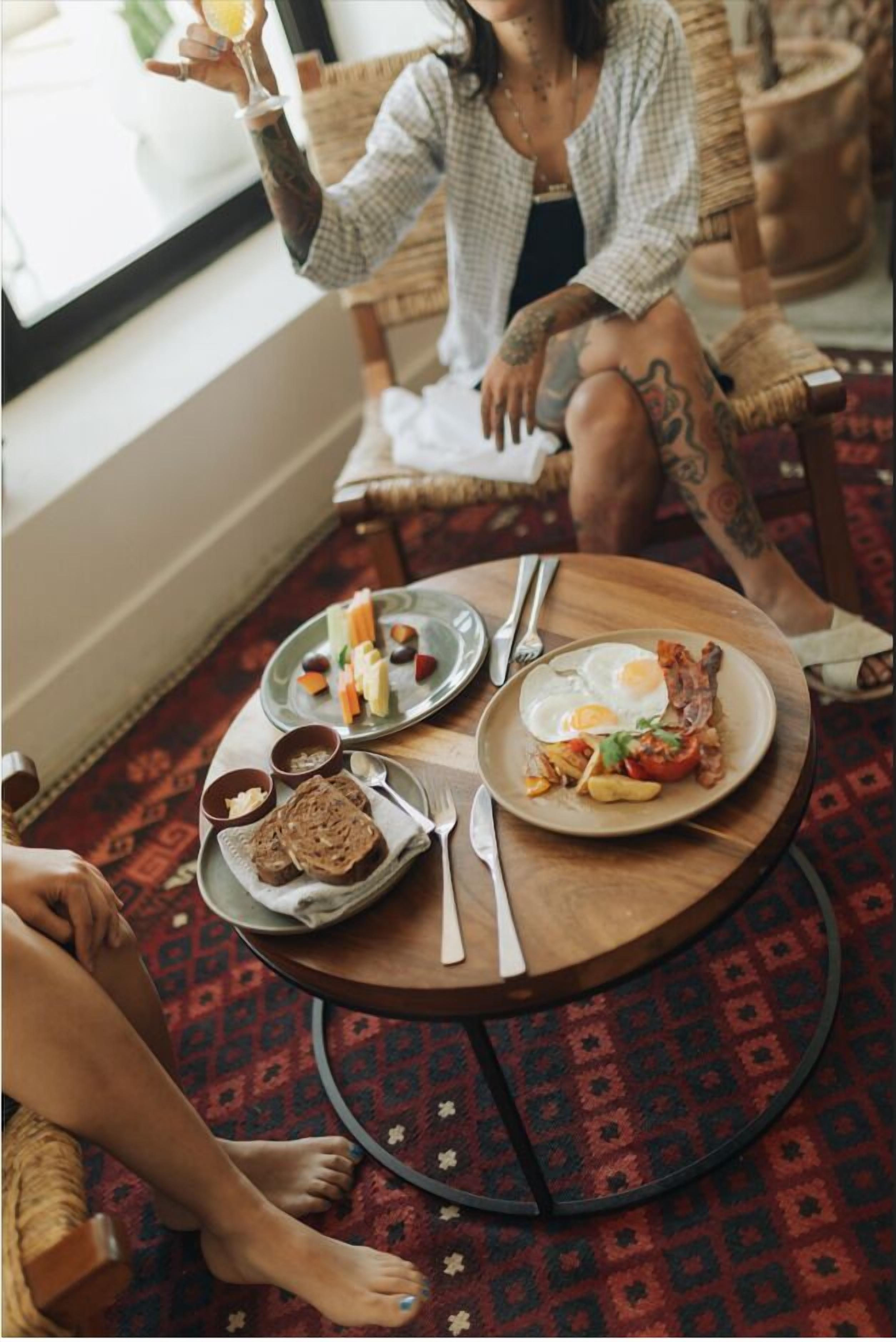 Et spiseområde med et rundt bord dækket til to personer, med tallerkener med æg, bacon og grøntsager, samt et glas appelsinjuice.