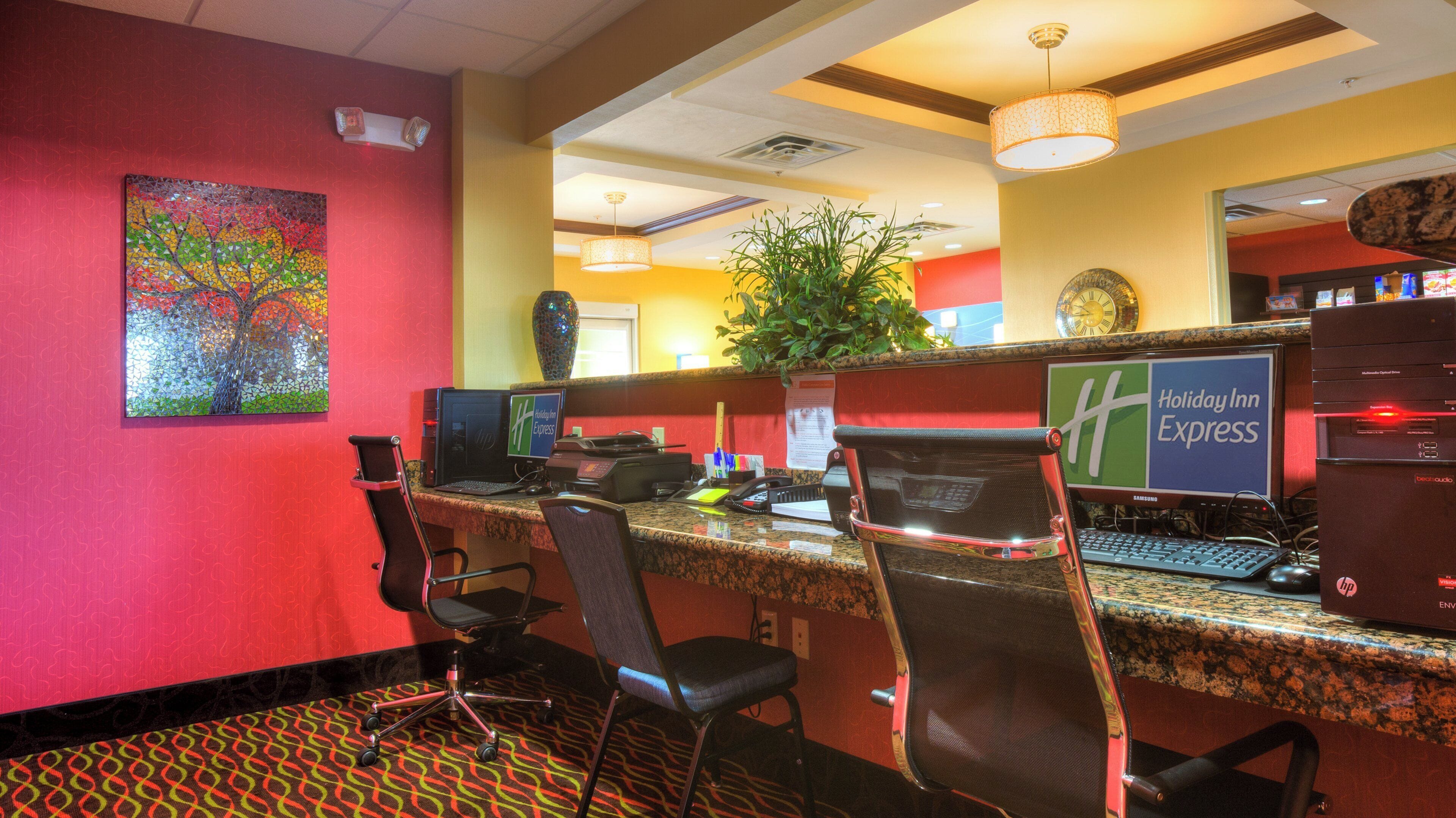 Balcão de recepção de hotel com computadores, uma planta e um quadro na parede.
