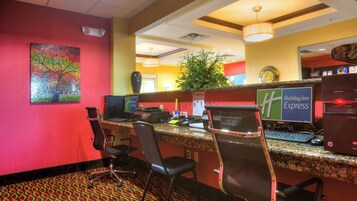 Un mostrador de recepción de hotel con computadoras, una planta y un cuadro en la pared.