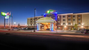 A Holiday Inn Express & Suites building with a covered entrance, multiple parking spaces, and flags.