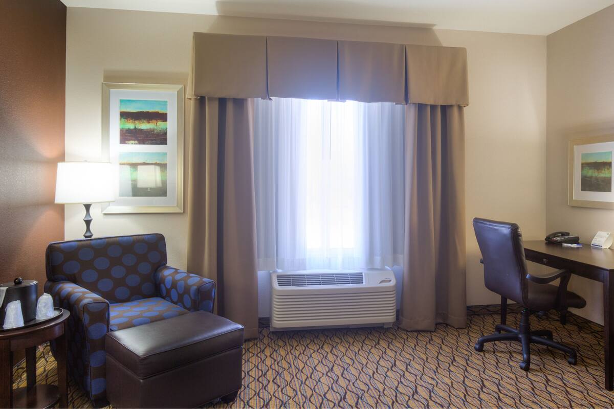 Ein Hotelzimmer mit Schreibtisch, Stuhl, Klimaanlage und einem gemusterten Teppich.