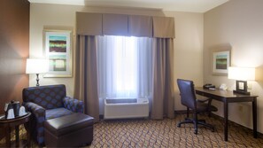 Ein Hotelzimmer mit Schreibtisch, Stuhl, Klimaanlage und einem gemusterten Teppich.