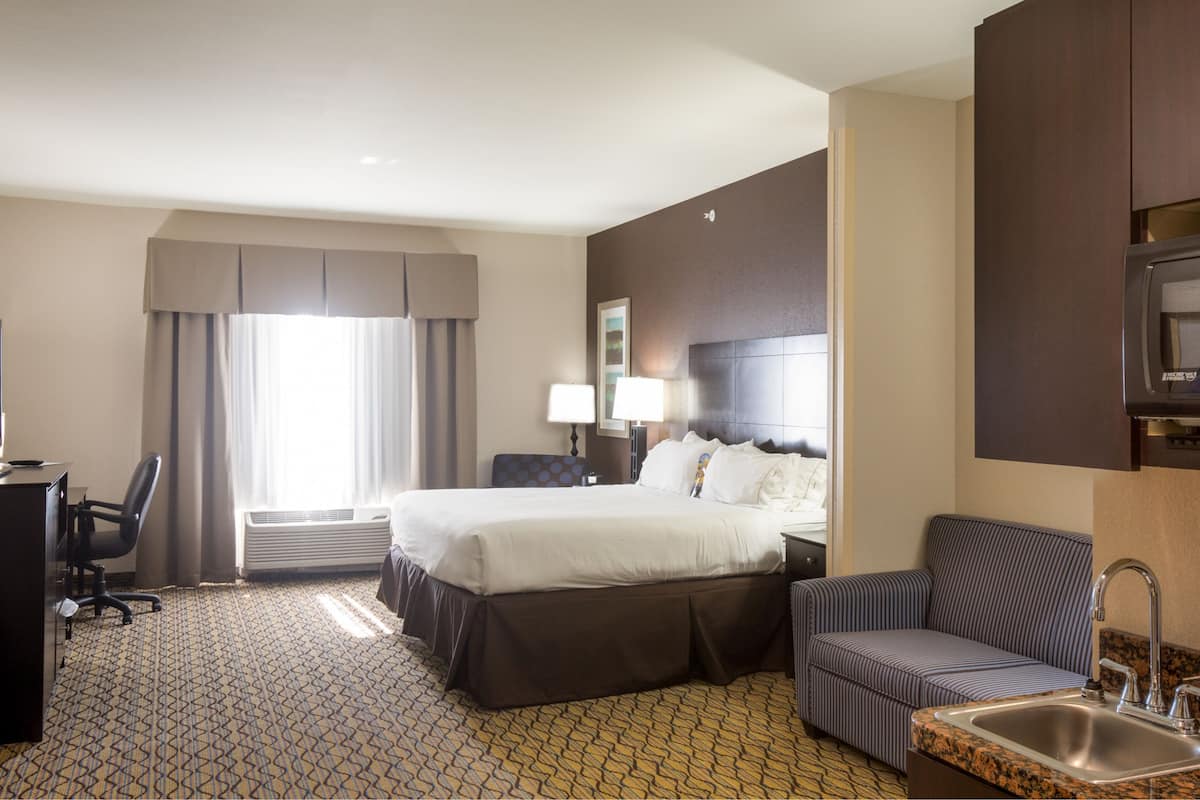 Ein Hotelzimmer mit einem Bett, einem Schreibtisch mit Computer, einem Sessel, einer Sitzecke, einer Mikrowelle und einem Waschbecken.