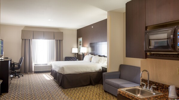 Ein Hotelzimmer mit einem Bett, einem Schreibtisch mit Computer, einem Sessel, einer Sitzecke, einer Mikrowelle und einem Waschbecken.