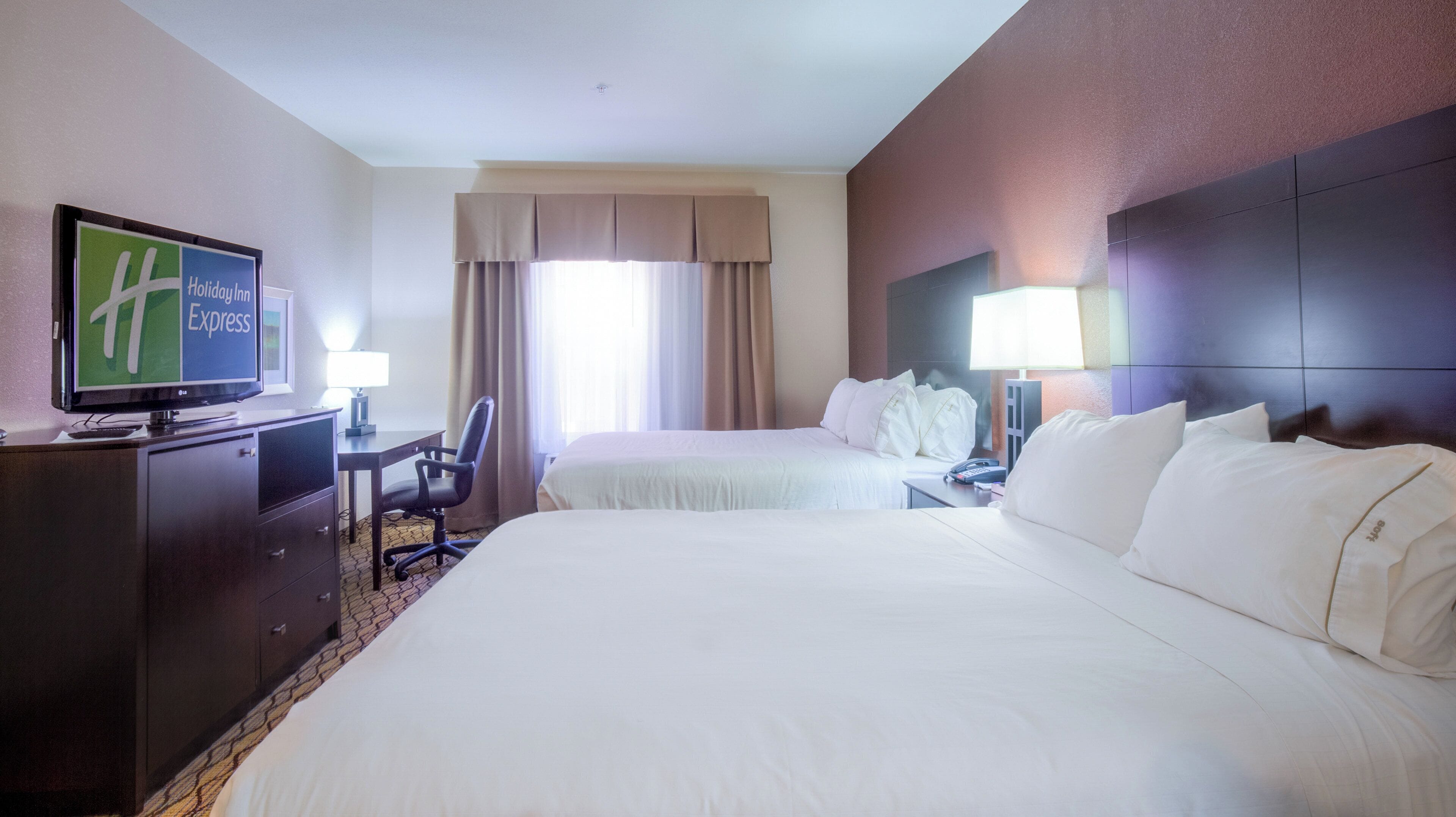 A hotel room with two beds, a desk with a chair, a television, and a nightstand with a lamp.