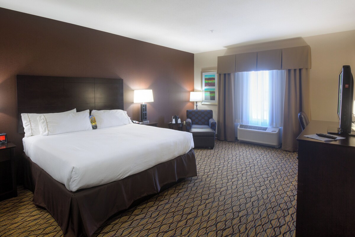 Ein Hotelzimmer mit einem großen Bett, einem Schreibtisch mit Computer, einem Sessel und einem Fernseher.