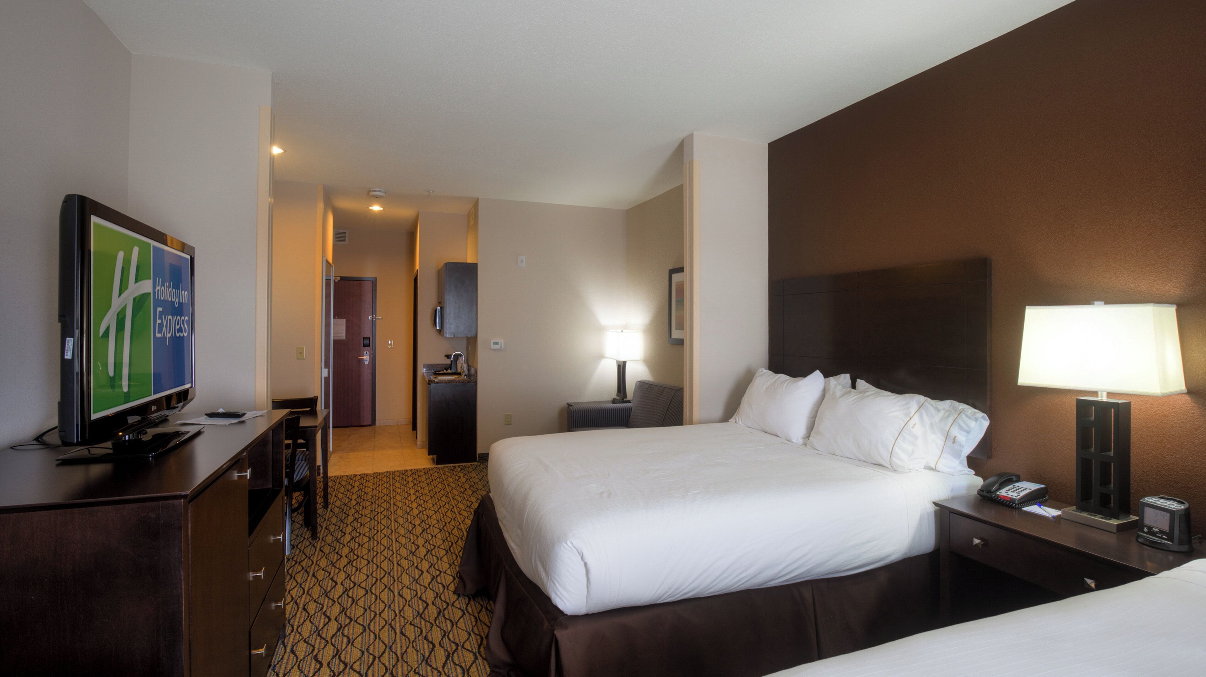 Habitació d'hotel amb llit, taulella de nit, làmpada, televisió i escriptori amb cadira.