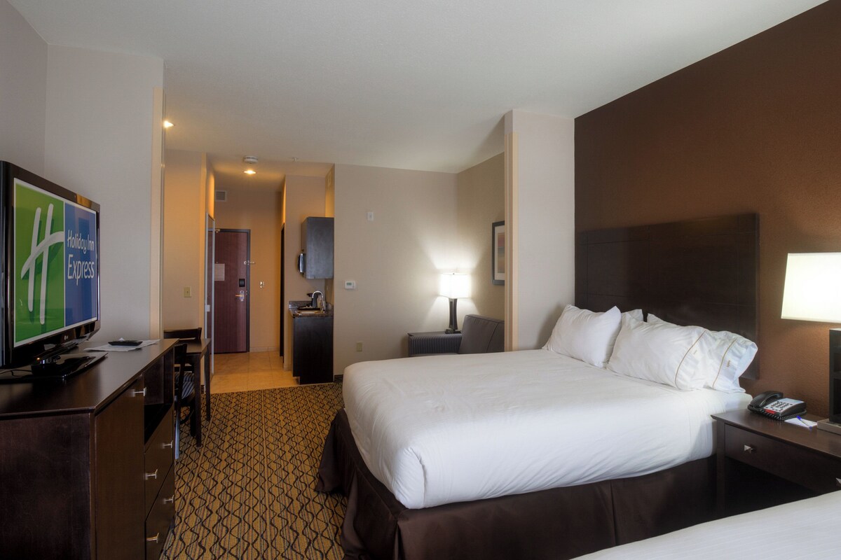 Ein Hotelzimmer mit Bett, Nachttisch, Lampe, Fernseher und Schreibtisch mit Stuhl.