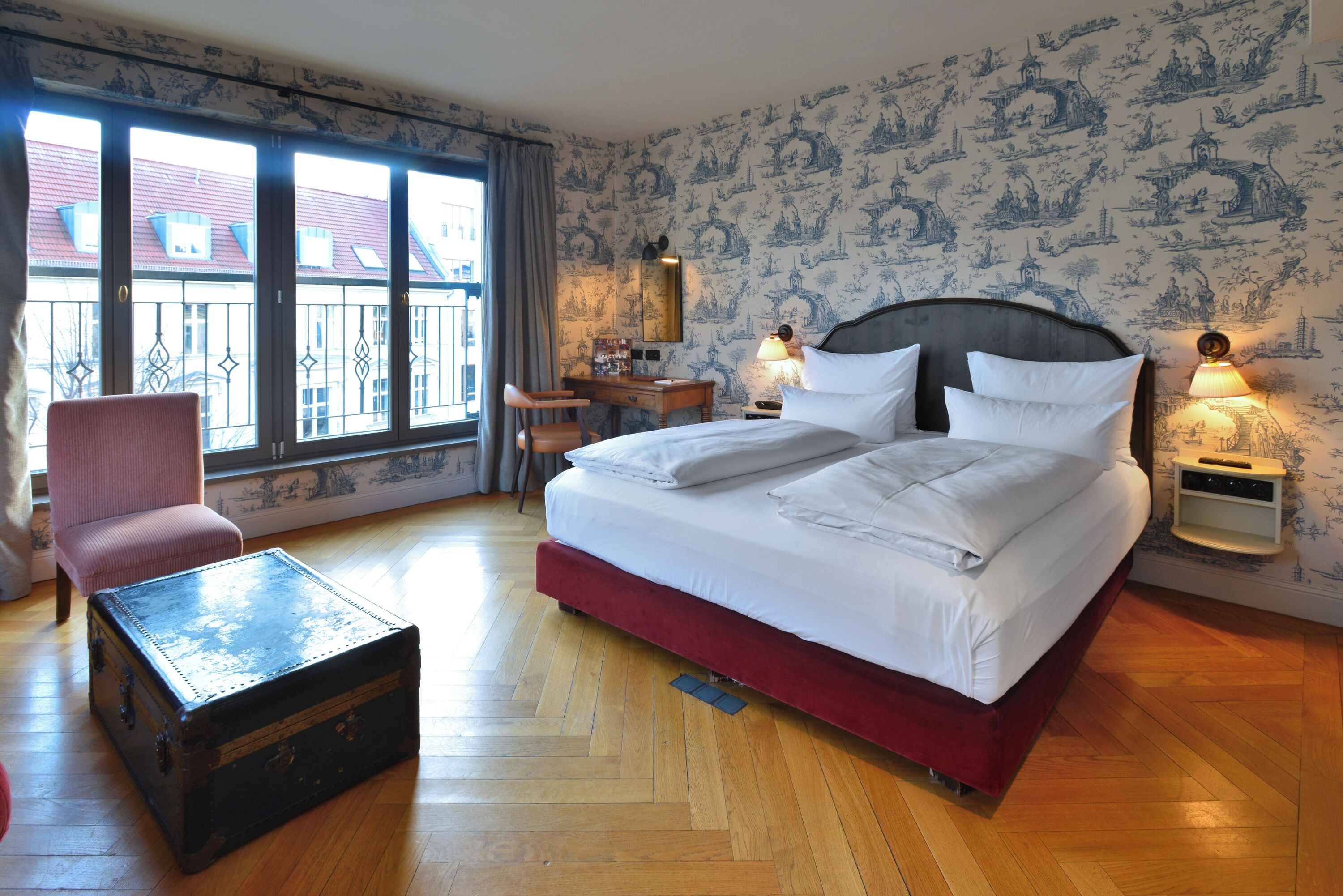 Une chambre d’hôtel avec un grand lit, un bureau, une chaise, une petite table et une valise.