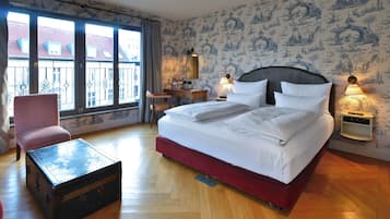 Quarto de hotel com cama grande, escrivaninha, cadeira, mesinha e mala.