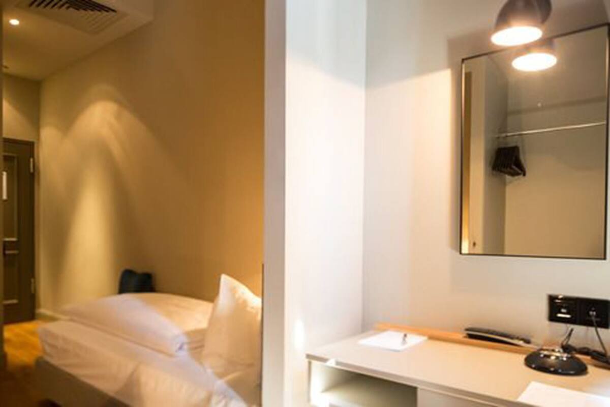 A hotel room with a bed, a desk with a computer, and a mirror on the wall.