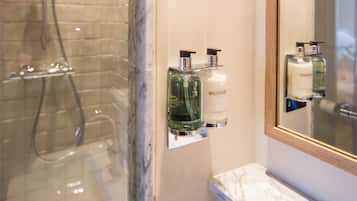 Un baño con mampara de vidrio, encimera de mármol y dos botellas de loción en un estante fijado a la pared.