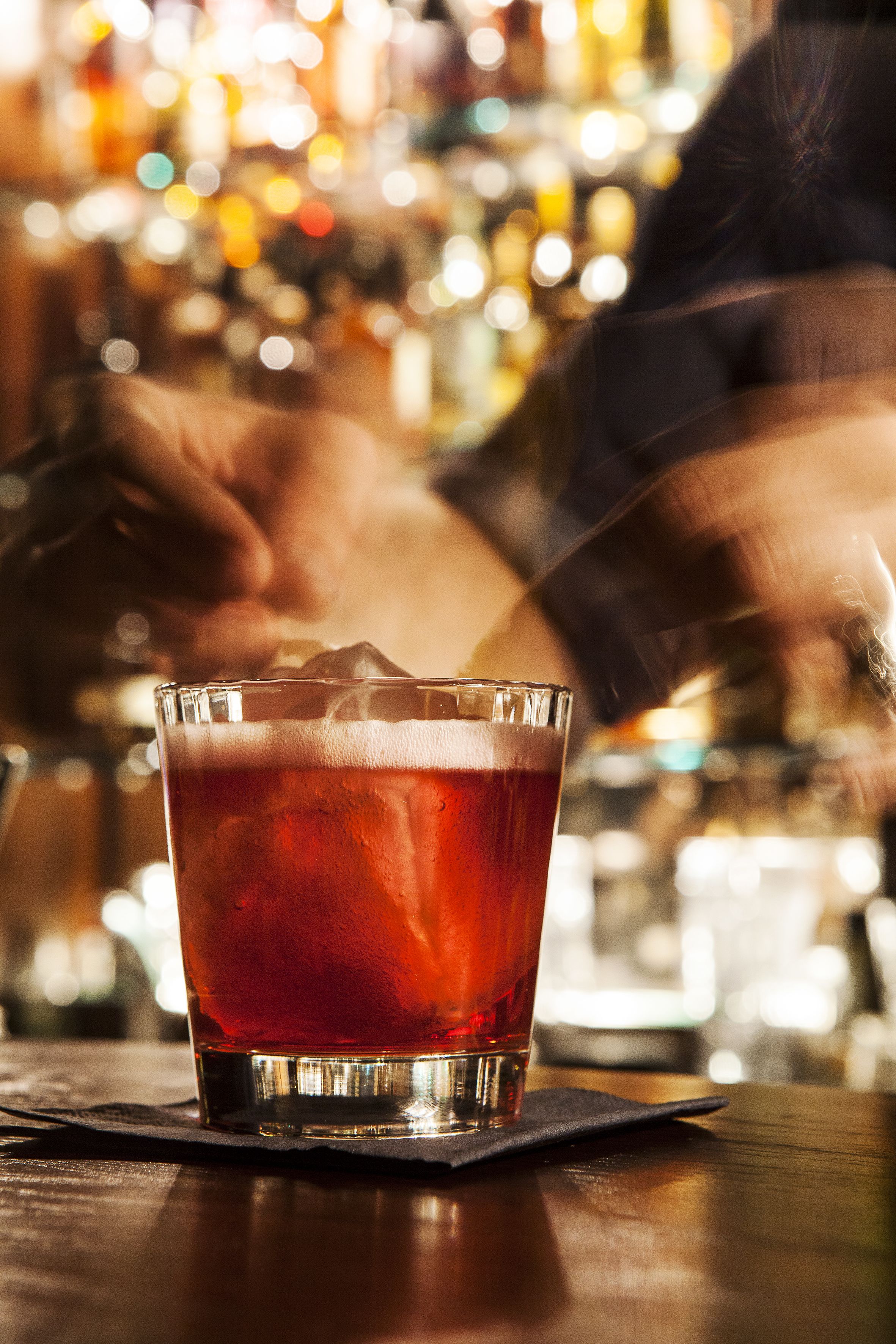 Un verre d’une boisson rouge est posé sur une table en bois, avec un arrière-plan flou représentant l’intérieur d’un bar.