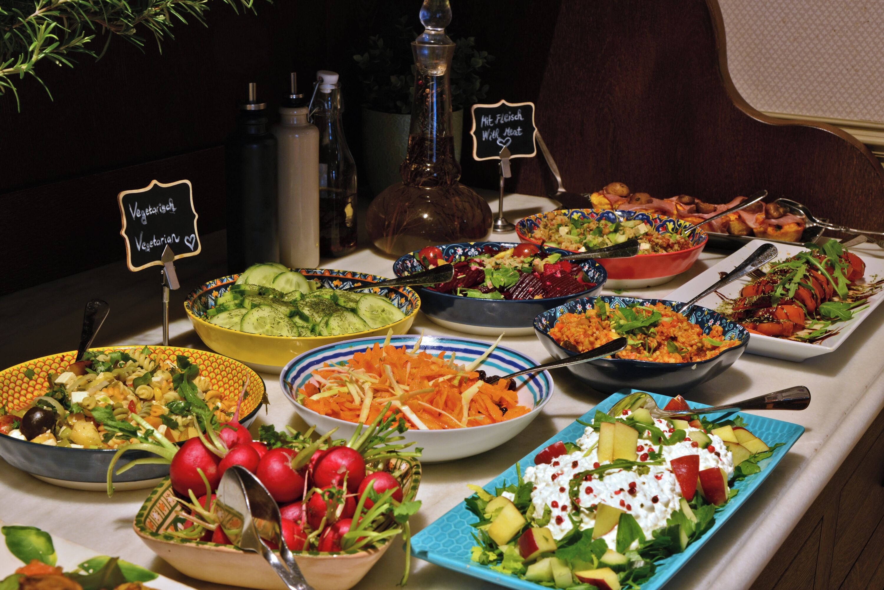 A buffet table with various dishes, including salads, vegetables, and a sign indicating vegetarian options.