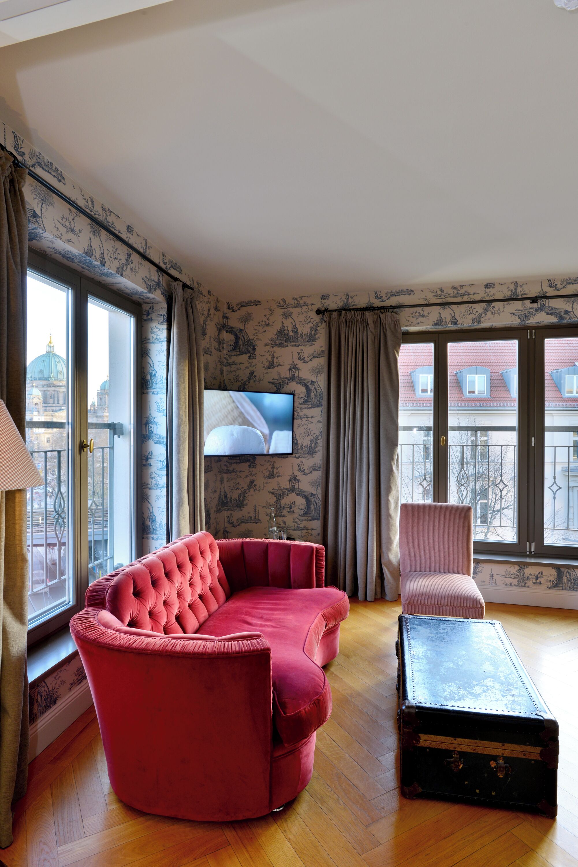Ein Wohnzimmer mit einem roten Sofa, einem rosa Sessel und einem schwarzen Koffer auf Holzdielen.