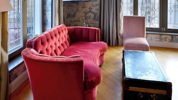 Ein Wohnzimmer mit einem roten Sofa, einem rosa Sessel und einem schwarzen Koffer auf Holzdielen.