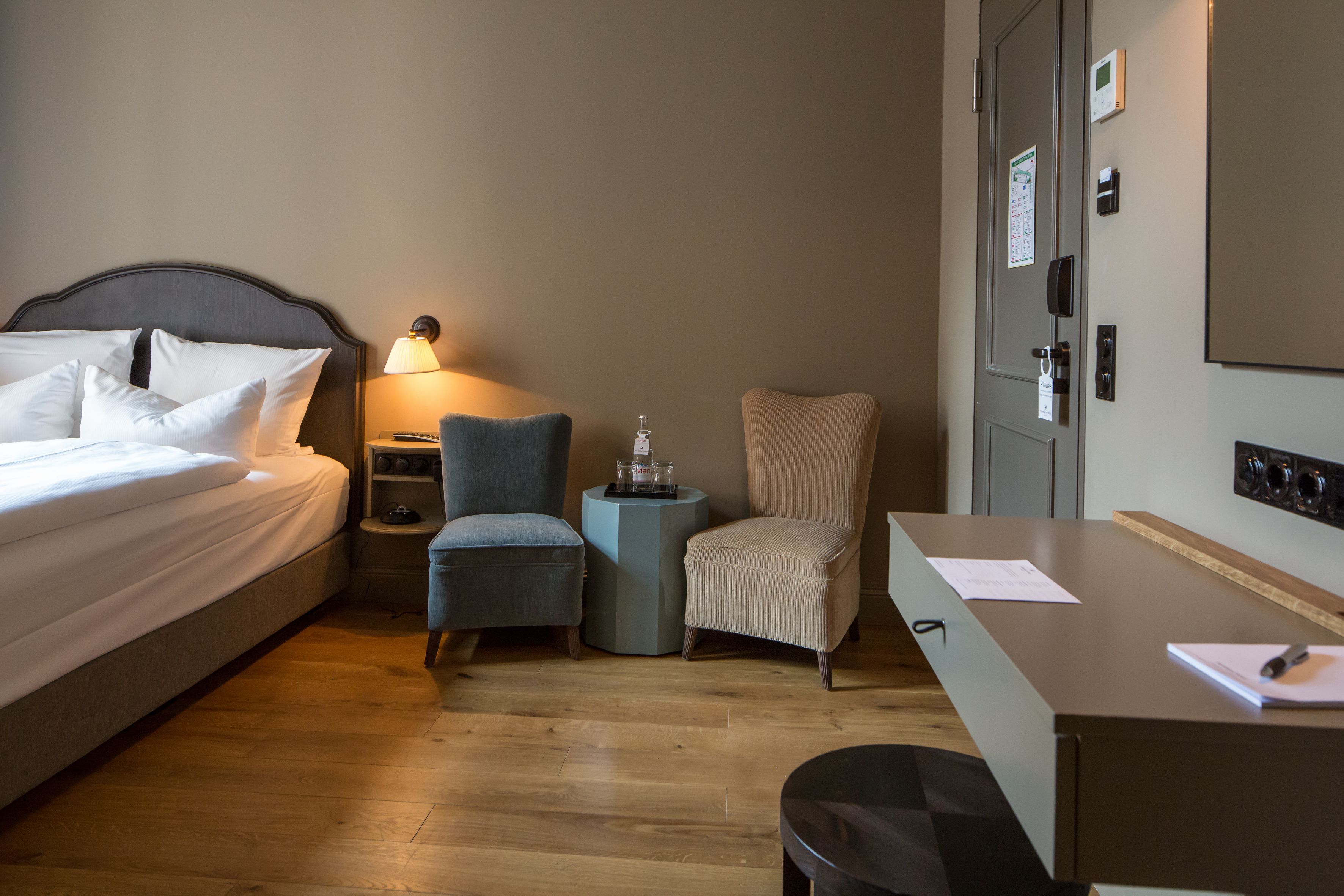 A hotel room with a bed, a desk, a chair, a nightstand, and a lamp.
