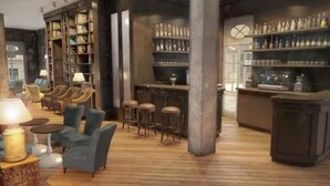 A bar area with shelves of bottles, a seating area with chairs and a table, and a bookshelf filled with books. - monbijou Hotel Berlin (Berlin)
