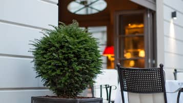 A potted plant, a chair, and a table outside a building with a window and a wall-mounted light.