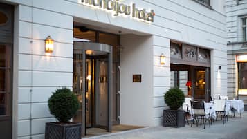 The exterior of the Monbijou Hotel with a glass entrance, outdoor seating area, and a sign above the entrance.