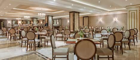 A spacious hotel lobby with multiple dining areas, chandeliers, and a large reception desk.