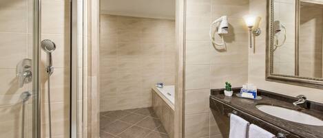 A modern bathroom with a glass-enclosed shower, a large mirror, and a marble countertop with a sink and towel rack.