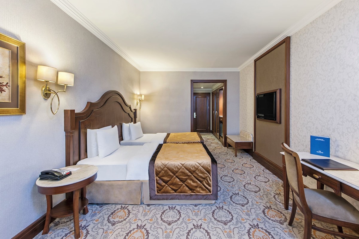A hotel room with a bed, bedside table, lamp, TV, desk, and chair.