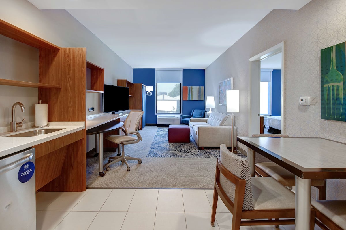 Una habitación de hotel moderna con una zona de cocina, una mesa de comedor, un sofá y un ventanal grande.
