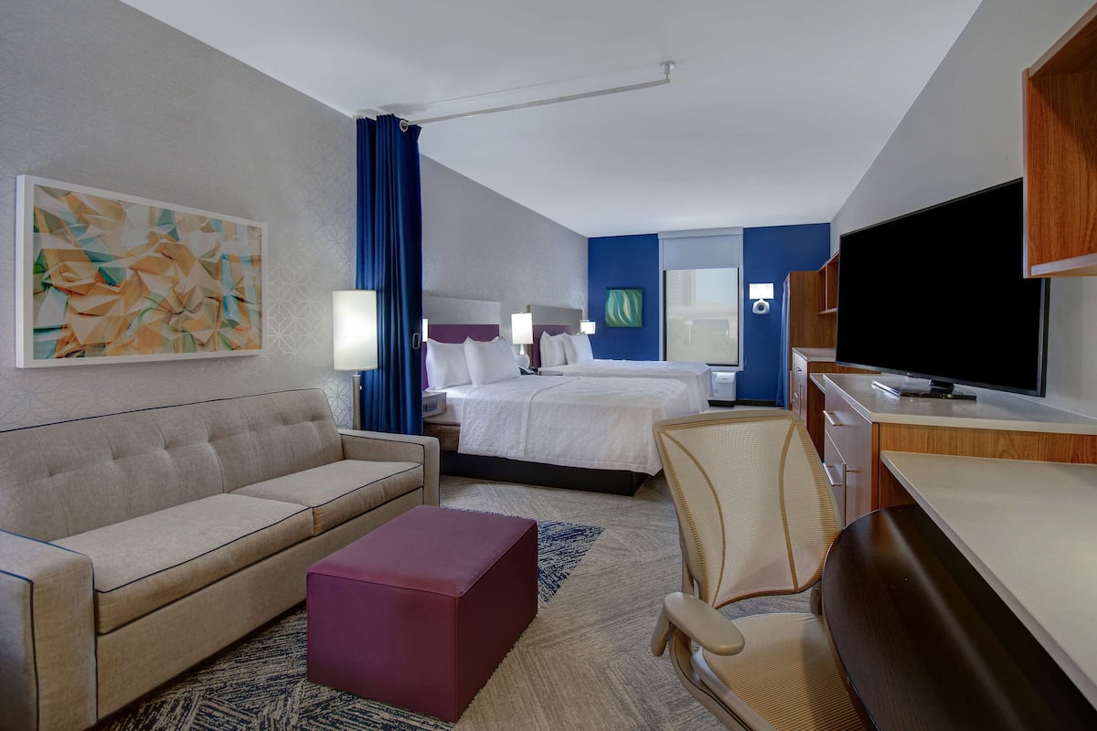 Habitación de hotel con cama, sofá, escritorio, televisión y un cuadro en la pared.