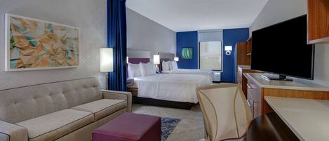 A hotel room with a bed, a sofa, a desk, a television, and a painting on the wall.
