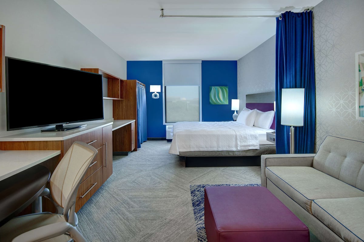 Una habitación de hotel con cama, escritorio con televisor, sofá y ventana con cortinas.