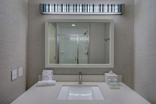 A modern bathroom with a large mirror, a sink, and a shower. - Home2 Suites by Hilton Dallas-Frisco (Frisco)