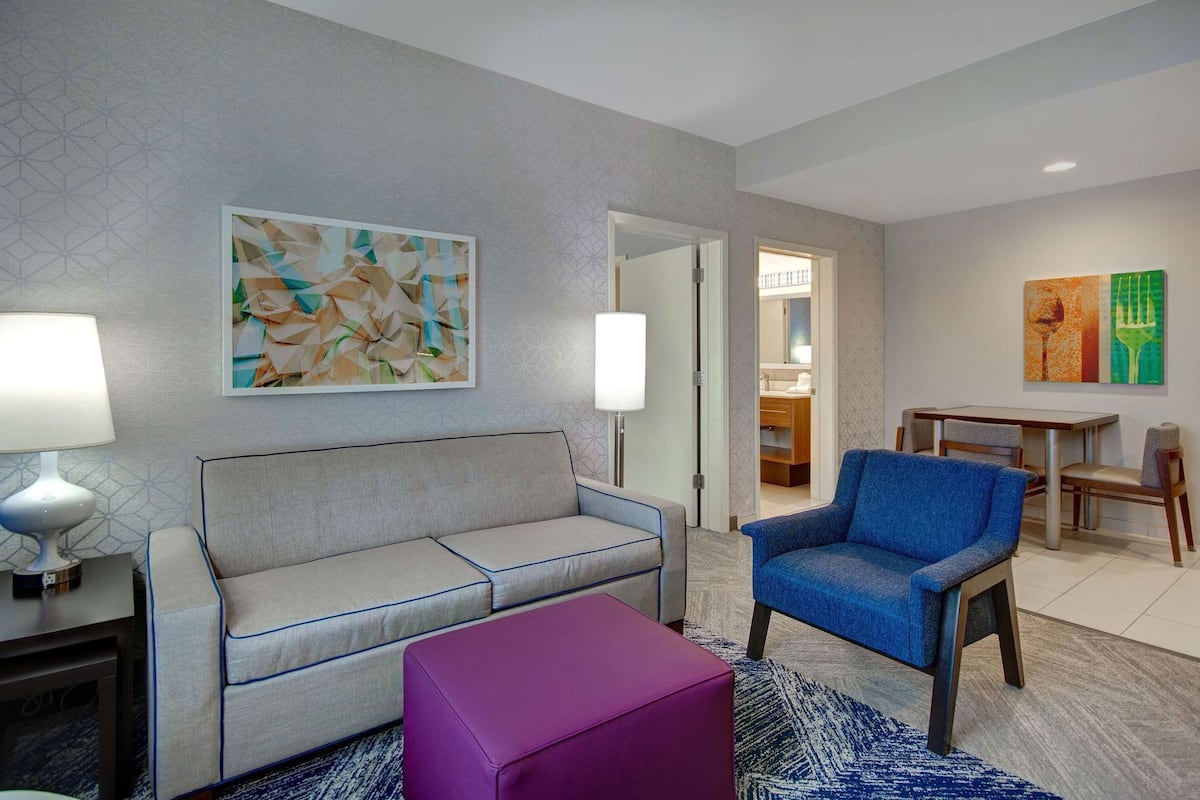 Una habitación de hotel moderna con un sofá, una silla, una mesita y un otoman púrpura.