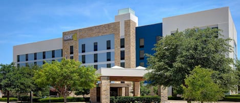 A multi-story hotel with a modern design, featuring a prominent sign, a covered entrance, and a parking lot.