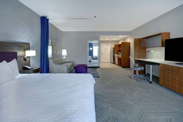 A hotel room with a large bed, a desk with a computer, a TV, and a kitchenette. - Home2 Suites by Hilton Dallas-Frisco (Frisco)