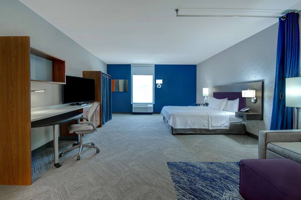 Una habitación de hotel con cama, escritorio, silla y un ventanal grande.