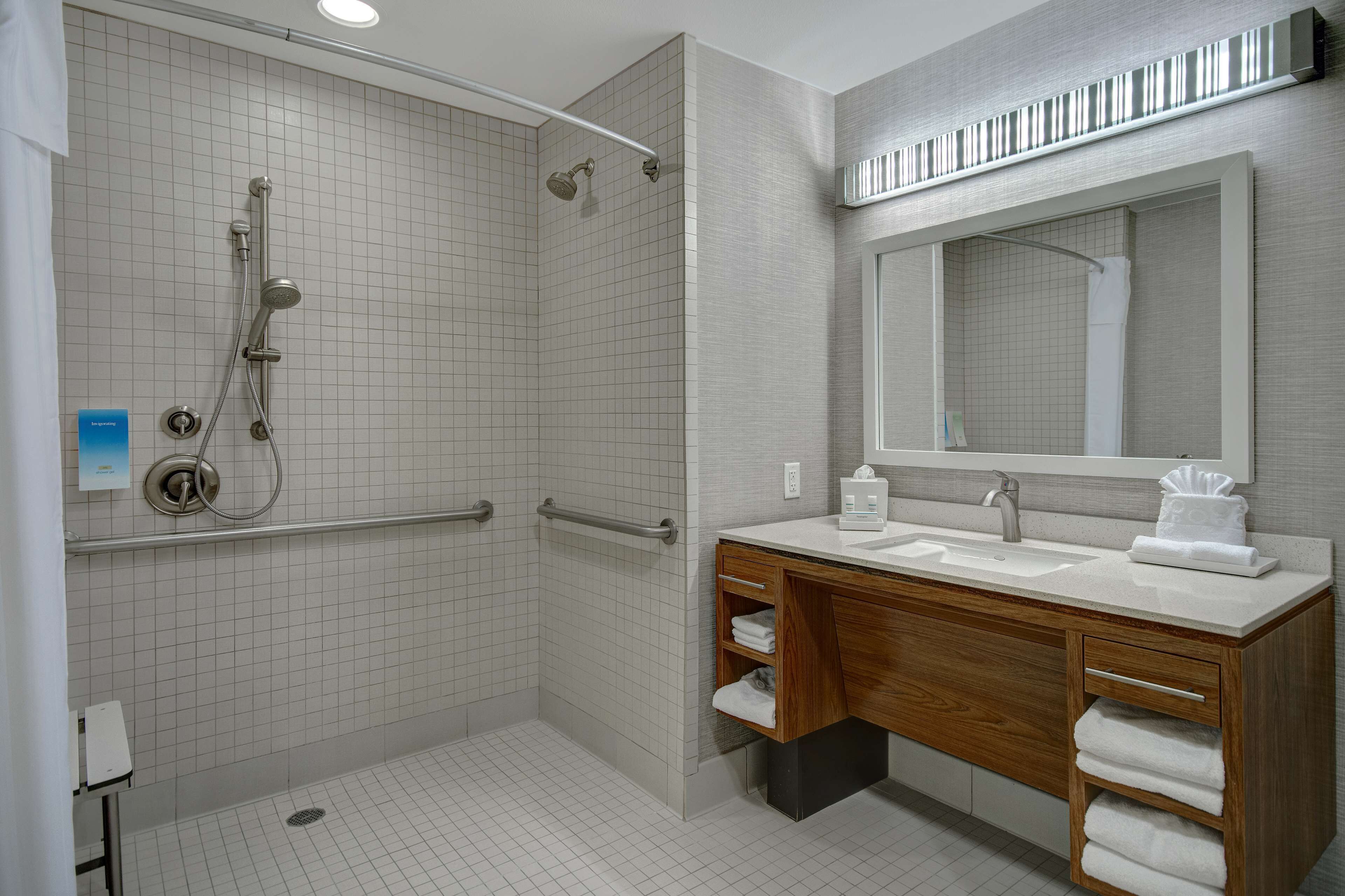 A modern bathroom with a walk-in shower, a wooden vanity with a sink, and a large mirror.