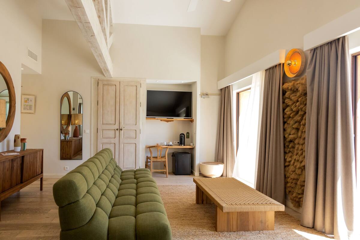 A living room with a green sofa, a wooden bench, a TV, a desk with a chair, and a large mirror.