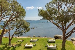 A serene lakeside setting with outdoor seating areas and large trees providing shade.