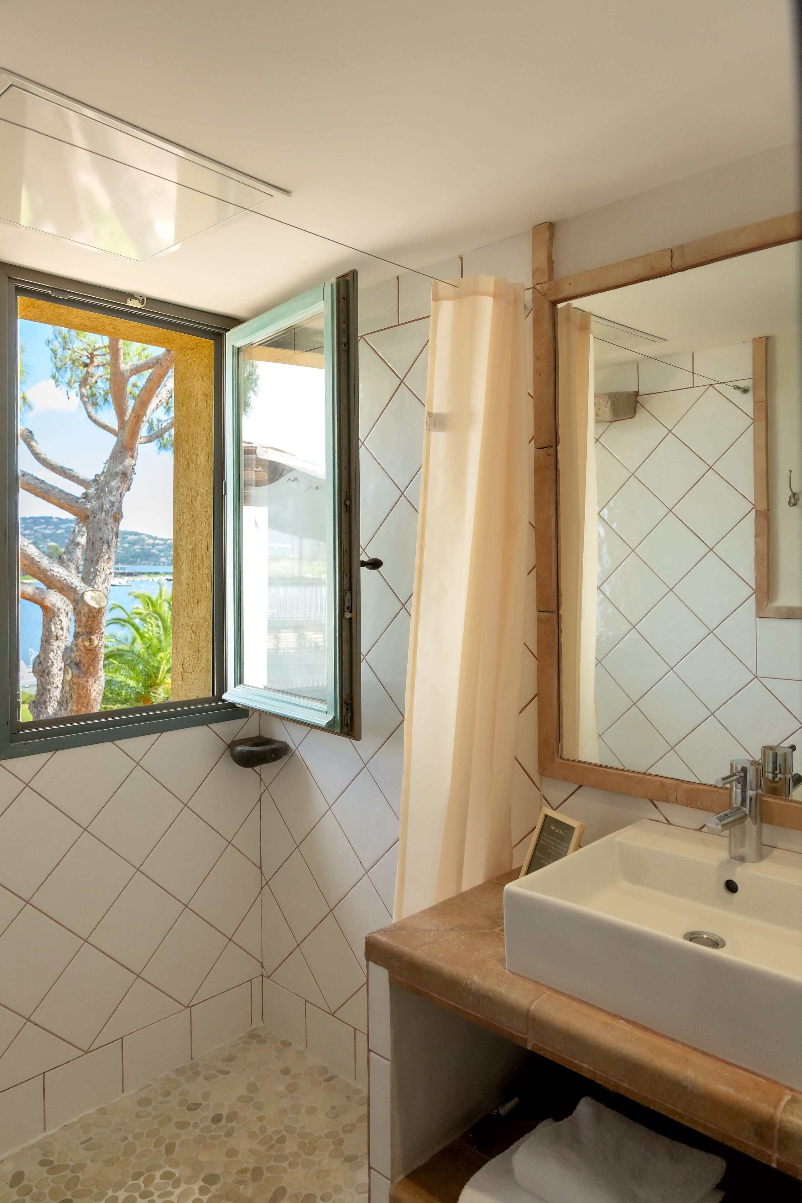 Een badkamer met een groot raam, een douche, een wastafel en een spiegel.