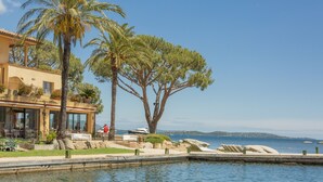 A waterfront property with a pool, palm trees, and a building with outdoor seating. - Casa Santini x Roc Seven (Porto-Vecchio)