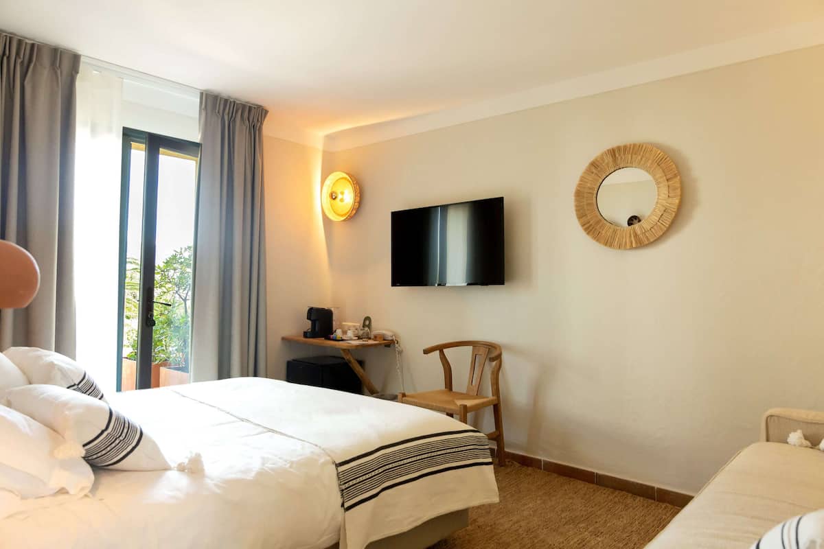 A hotel room with a bed, a chair, a desk with a computer, a TV, and a window with curtains.