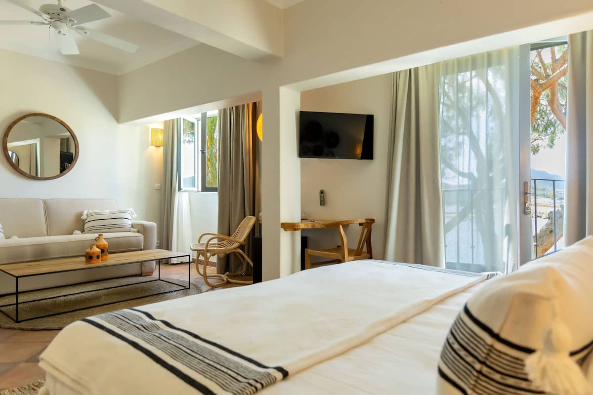 A hotel room with a bed, a sofa, a coffee table, a TV, and a balcony with a view.