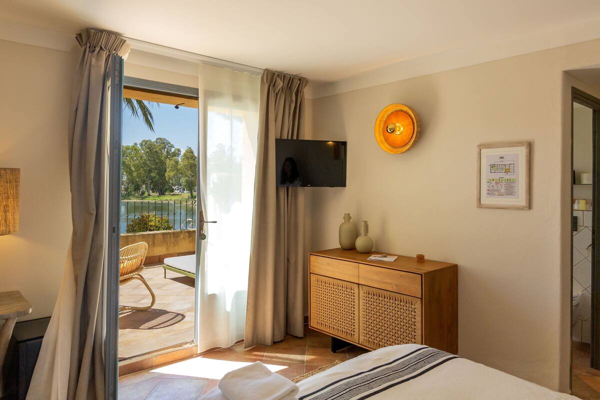 A hotel room with a bed, a TV mounted on the wall, a wooden cabinet, and a balcony with a chair.