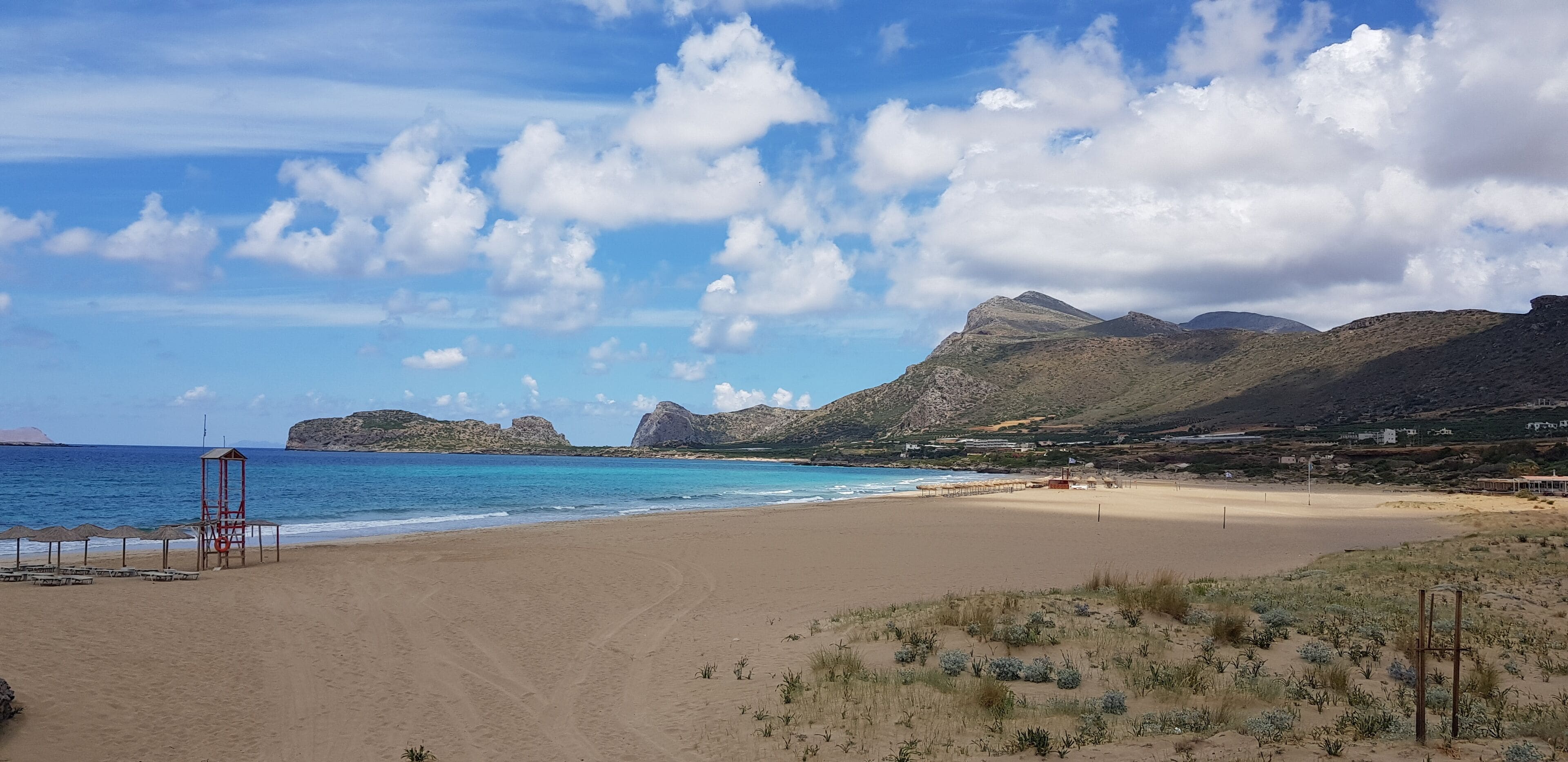 A beach with clear blue water, sandy shore, and mountains in the background.