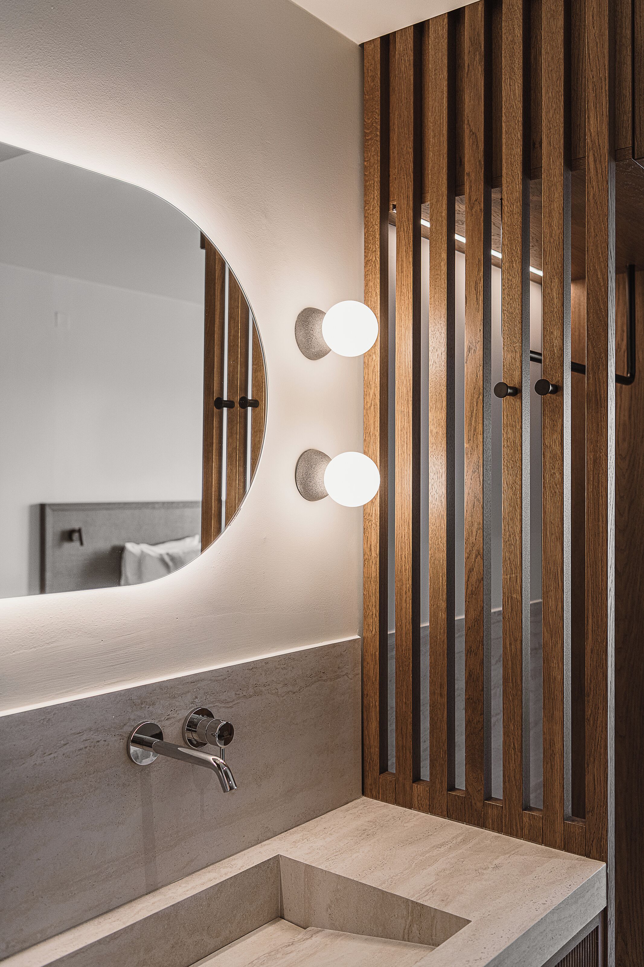 A bathroom with a large mirror, two round lights, a faucet, and wooden slats.
